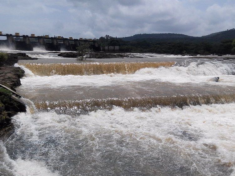 A close-up view of the water rushing over the Khadakwasla Dam. The water is a deep brown color, likely due to sediment, and is churning and bubbling as it flows over the dam.